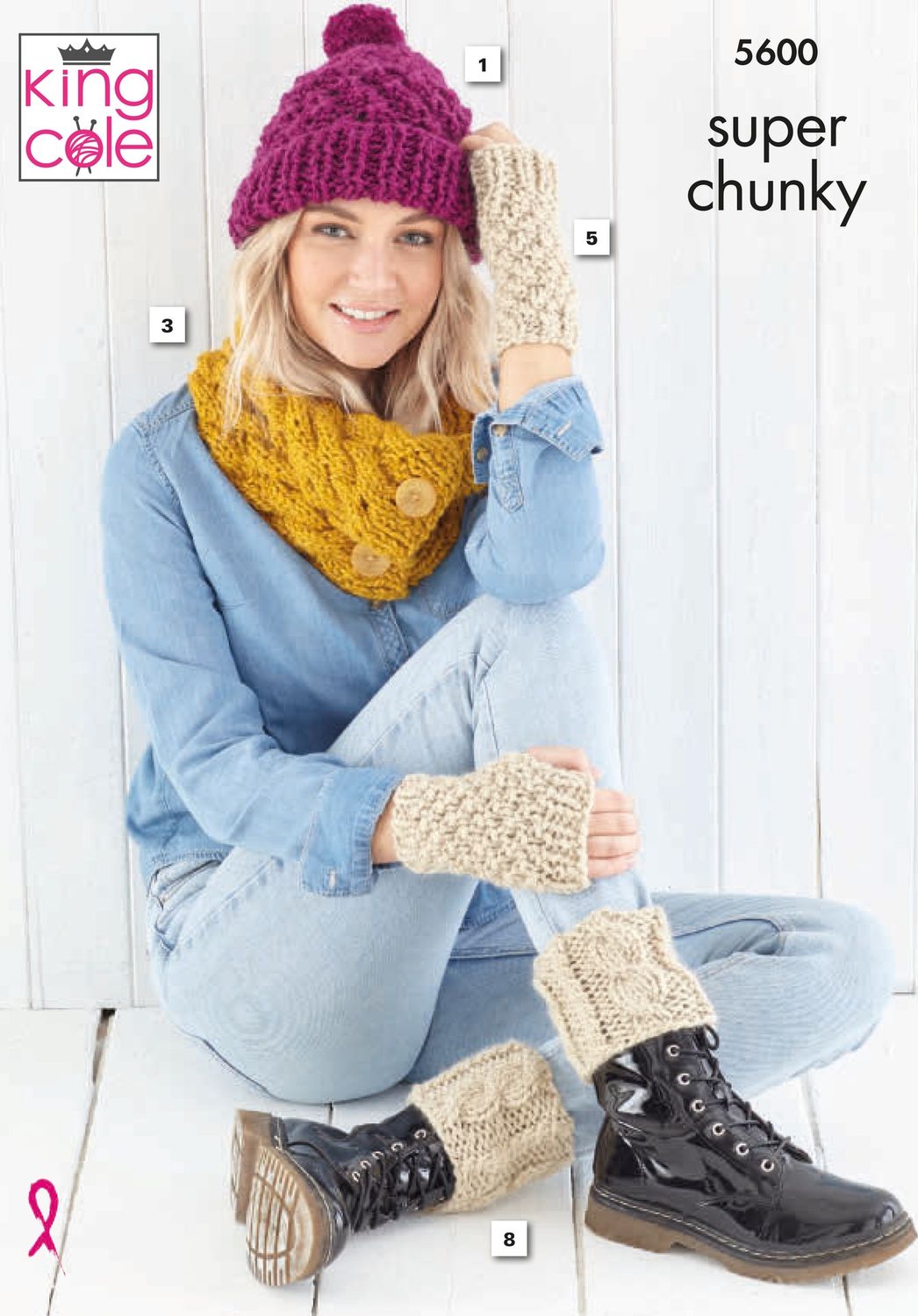 A woman is wearing a knitted hat in dark pink, a knitted cowl in yellow and knitted wrist and boot toppers in a dark cream.