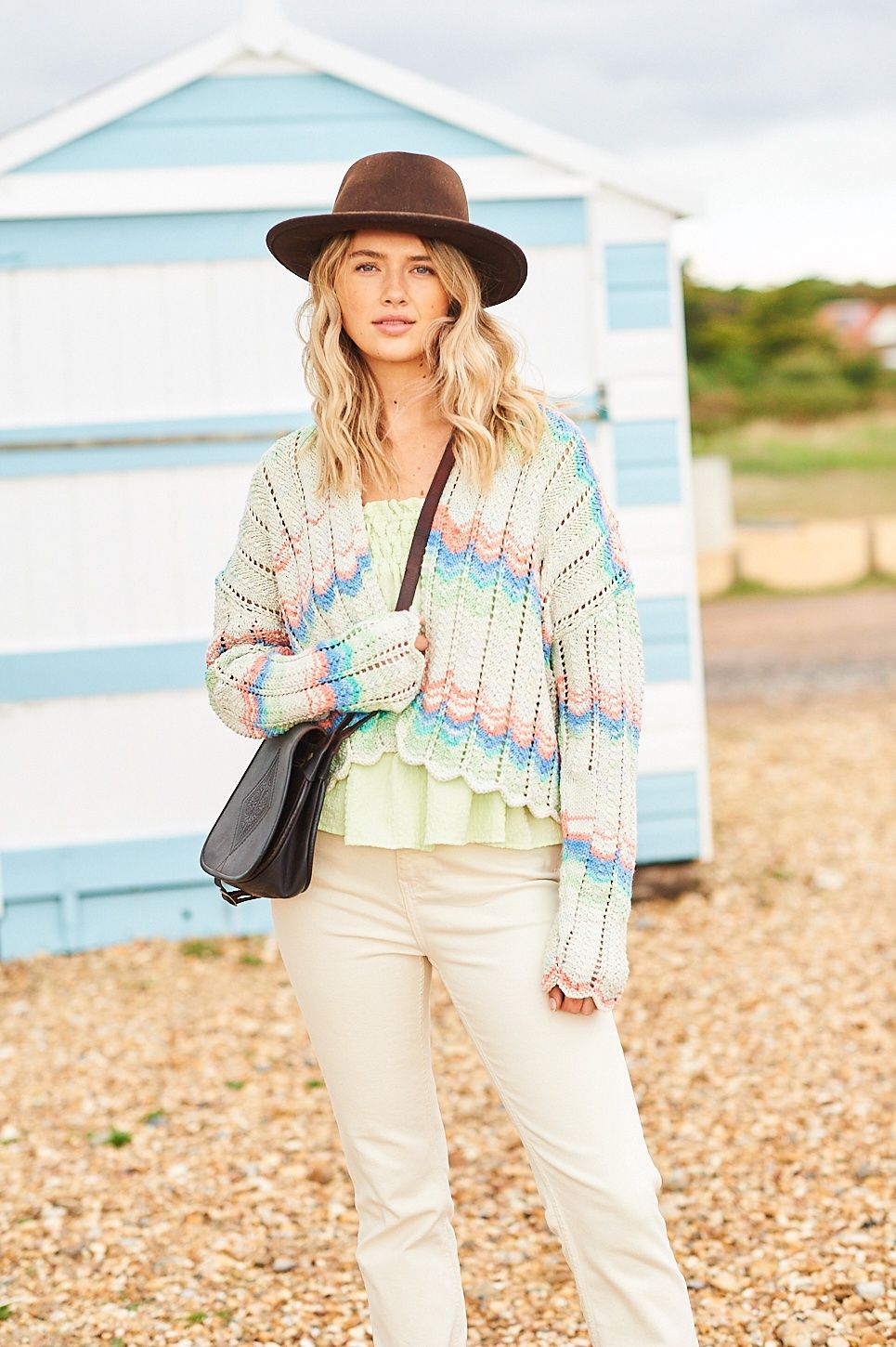 A woman is wearing a knitted wavy cardigan in shades of cream, peach, blue and green.