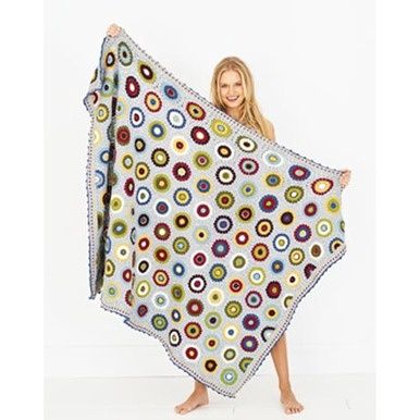 A woman is holding a crocheted blanket in grey, cream, yellow, green, purple, blue and red.