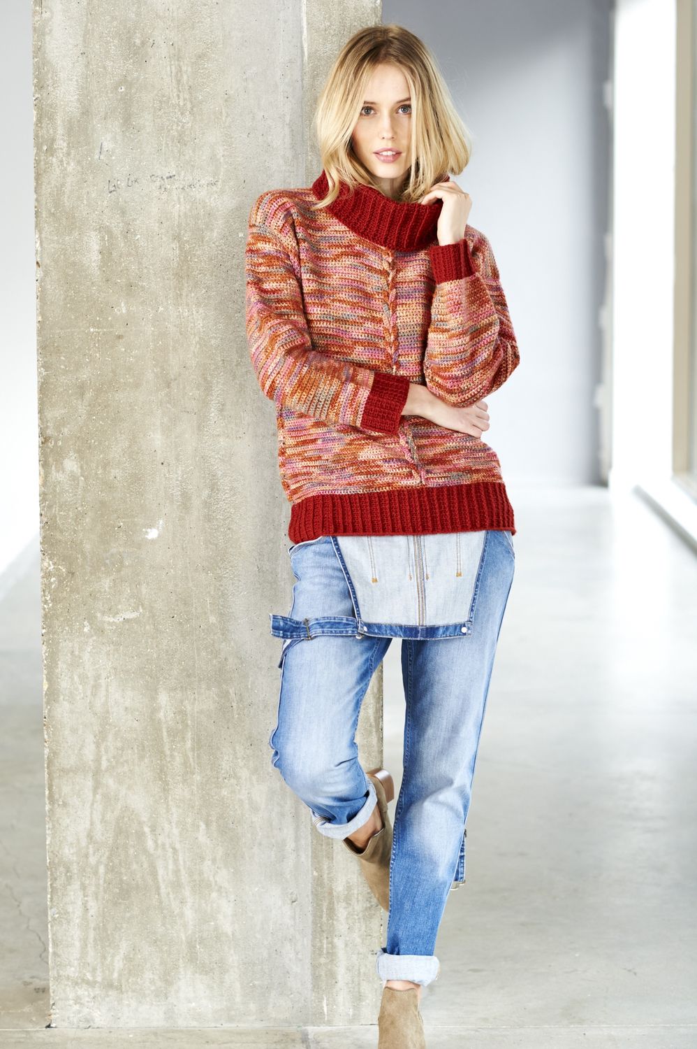 A woman is wearing a crocheted sweater in a variegated orange yarn.