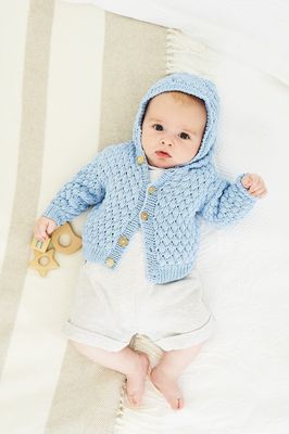 A baby is wearing a pale blue knitted cardigan.