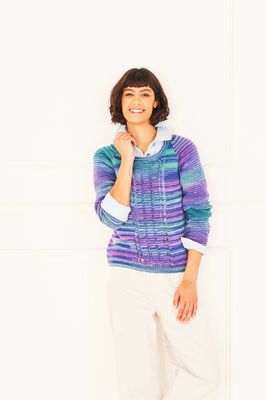 A woman is wearing a knitted sweater in shades of purple, blue and green.