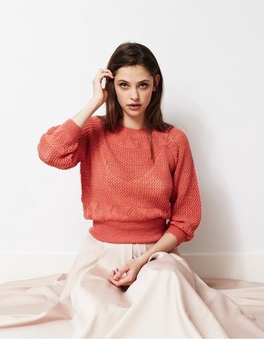A woman is wearing a red knitted sweater with diamond lace detail.