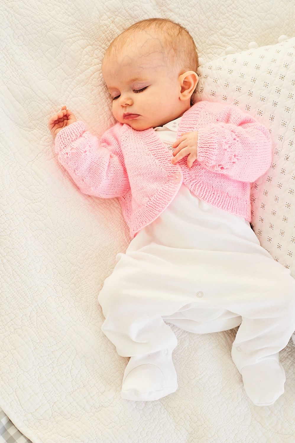 A baby is wearing a pink knitted cardigan.