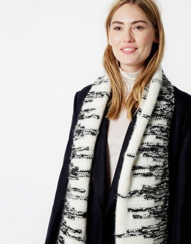 A woman is wearing a variegated black and white knitted scarf.