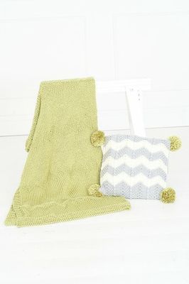 A pale green knitted blanket, and a grey and white chevron knitted cushion with green pompoms on each corner.