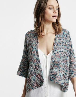 A woman is wearing a knitted cardigan in a variegated blue and brown yarn.