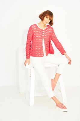 A woman is wearing a coral coloured crocheted cardigan.