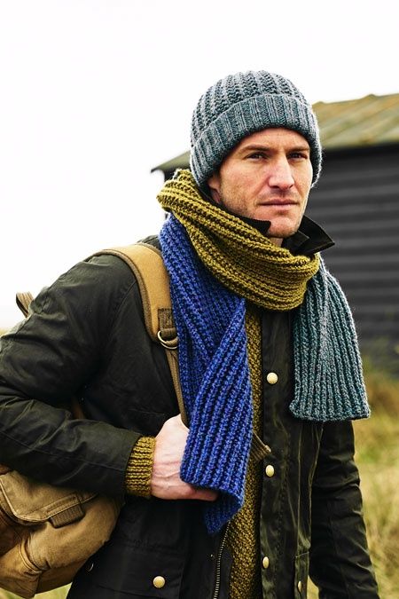 A man is wearing a teal hat and a teal, blue and green scarf.
