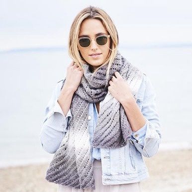 A woman is wearing a knitted scarf in a variegated grey and cream yarn.