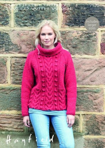 A woman is standing against a wall wearing a red cable knit sweater.