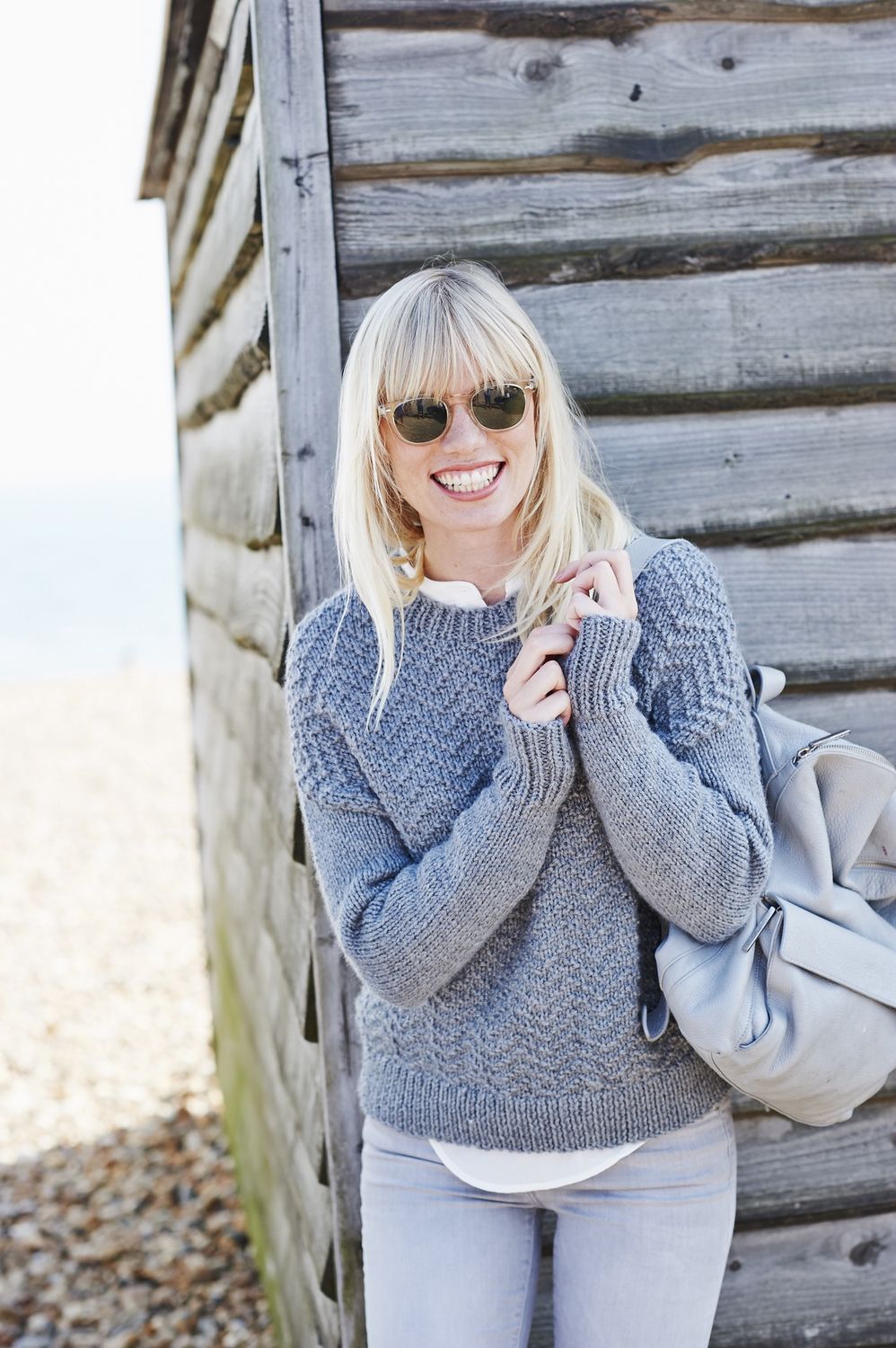 A woman is wearing a grey knitted sweater with a textured zigzag detail.