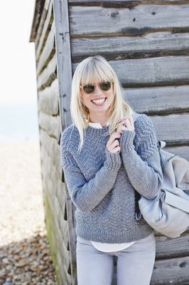A woman is wearing a grey knitted sweater with a textured zigzag detail.