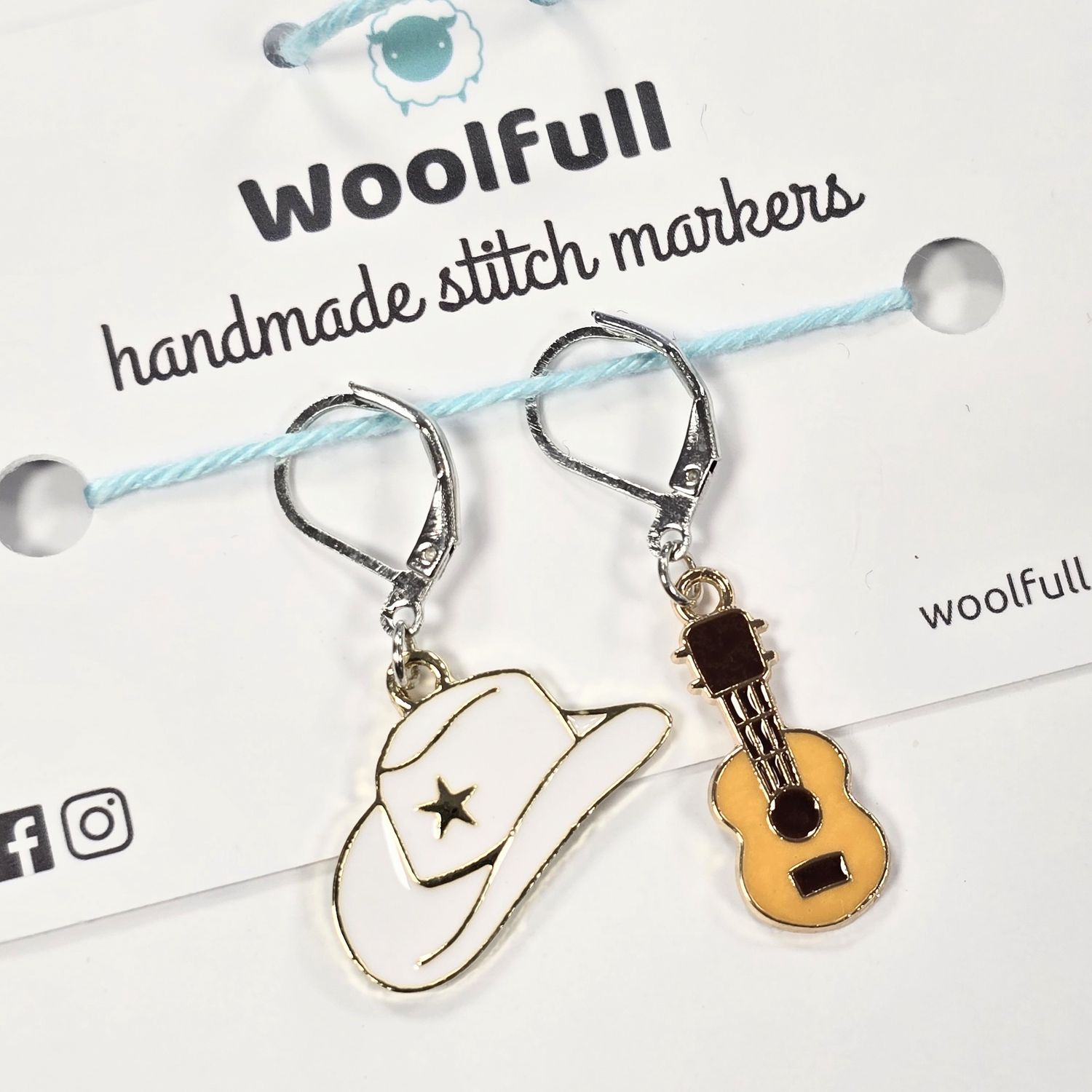 A white cowboy hat shaped stitch marker and a light brown guitar shaped stitch marker.
