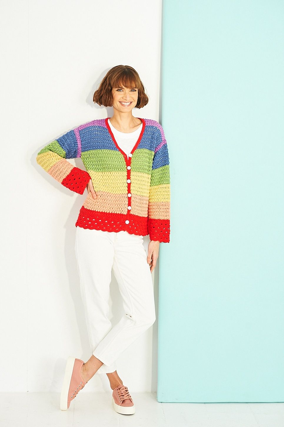 A woman is wearing a rainbow striped crocheted cardigan.