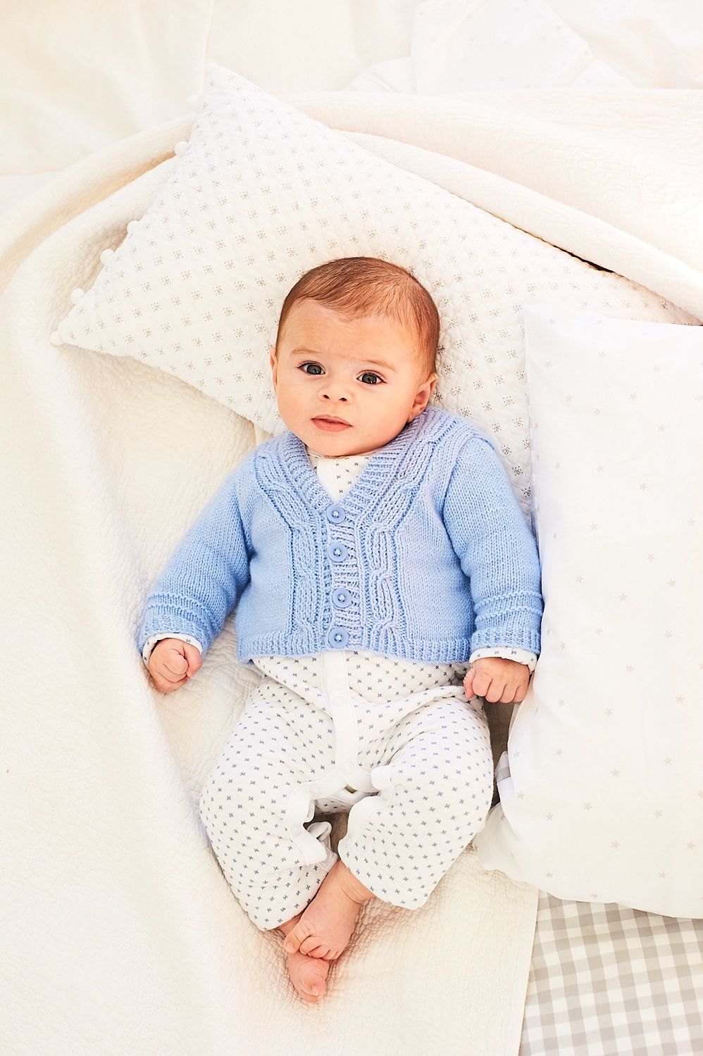 A baby is wearing a blue cable knit cardigan.