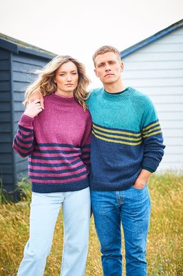 A woman is wearing a pink knitted sweater with navy blue stripes and a man is wearing a navy blue knitted sweater with green stripes.