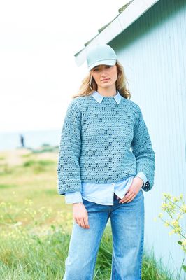 A woman is wearing a blue crocheted jumper with lace detail.