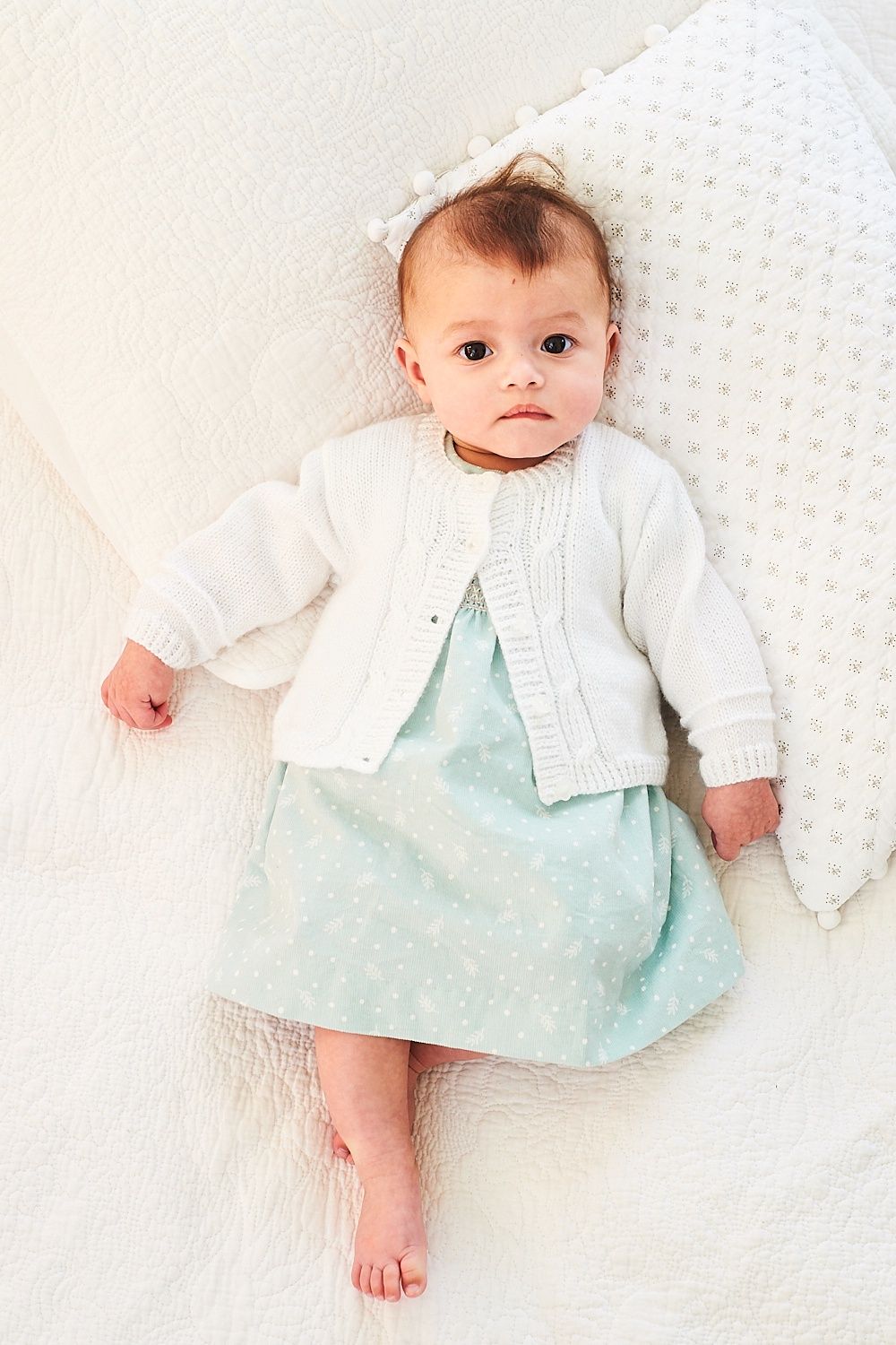A baby is wearing a white cable knit cardigan.