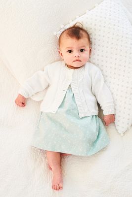 A baby is wearing a white cable knit cardigan.