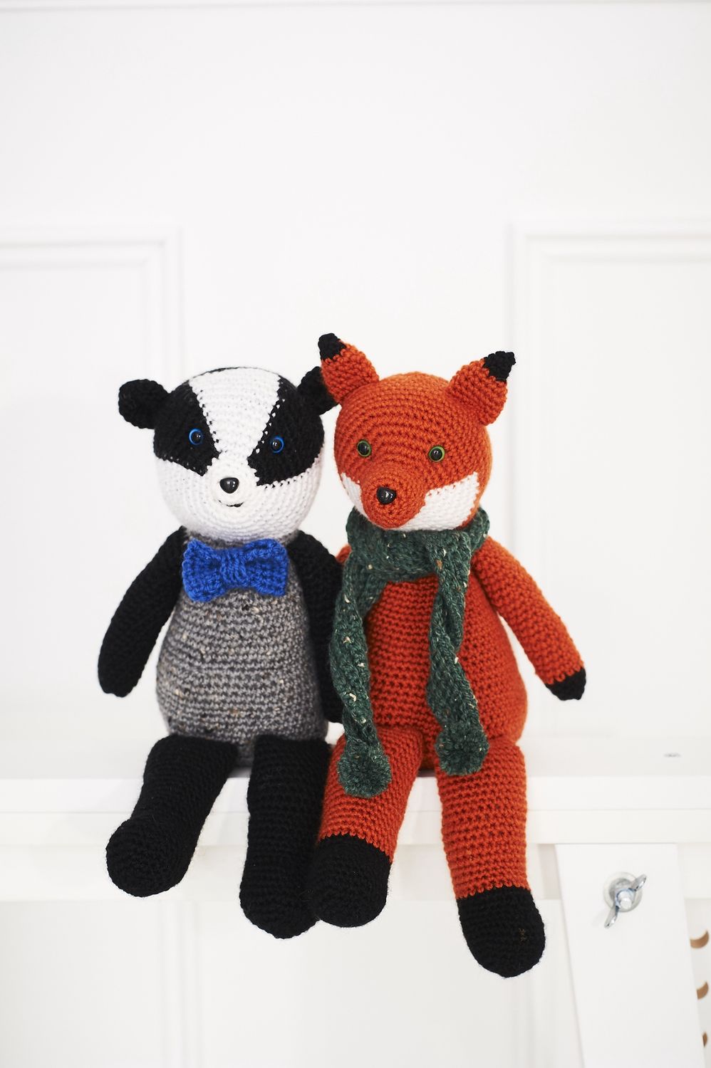 A crocheted badger in a blue bow tie sits alongside a crocheted fox in a green scarf.