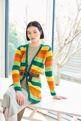 A woman is wearing an stripy knitted cardigan in shades of yellow, green and orange.