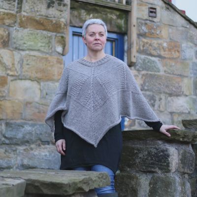 A woman is wearing a knitted pale grey poncho.
