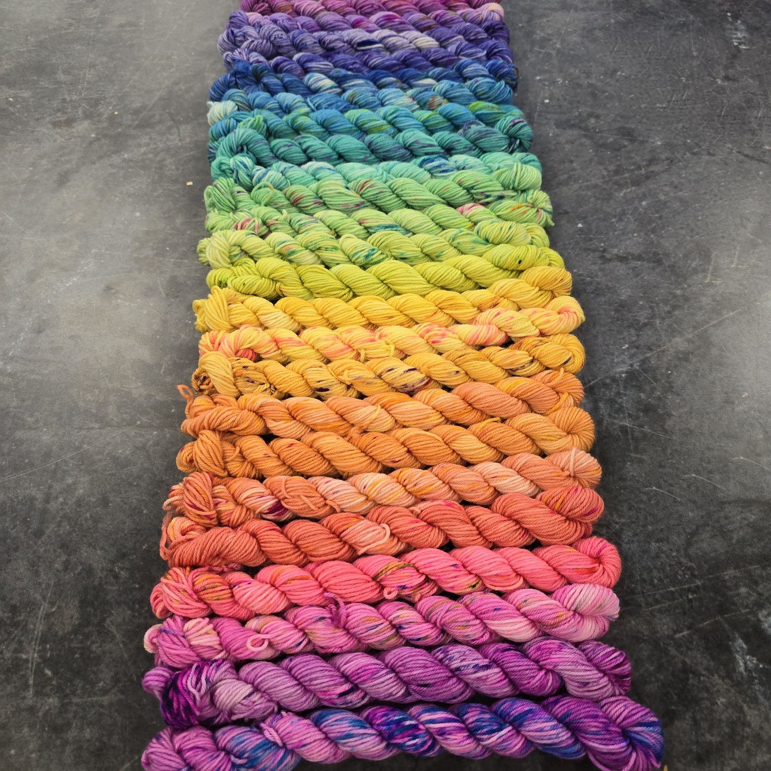 24 hand dyed mini skeins laid out in a bright rainbow gradient.