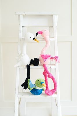 A pink crocheted flamingo, a white with black crocheted swan and a blue and green crocheted duck.