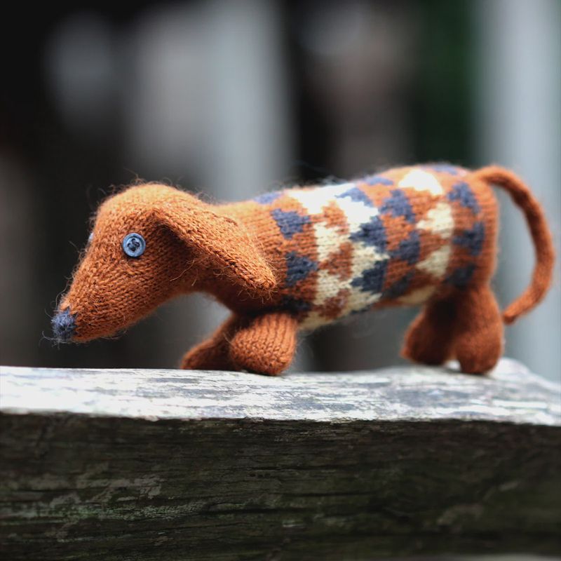 A knitted dachshund toy in shades of brown, grey and cream.