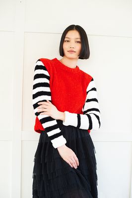 A woman is wearing an red knitted sweater with black and white stripy sleeves.