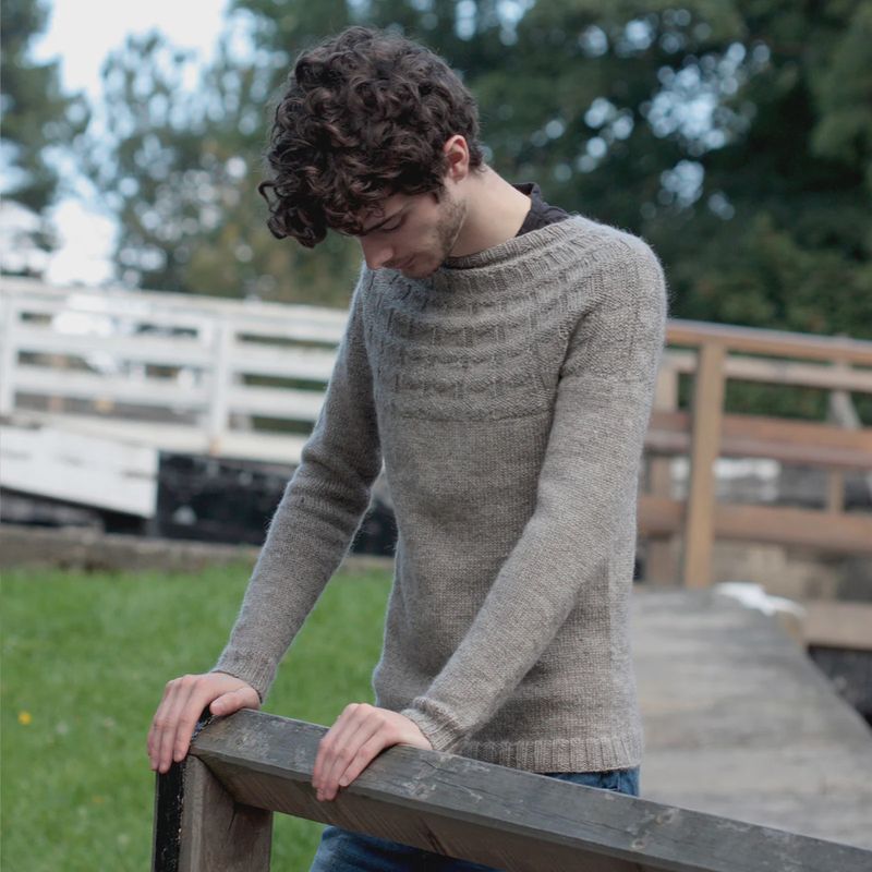 A man is wearing a knitted pale grey sweater.