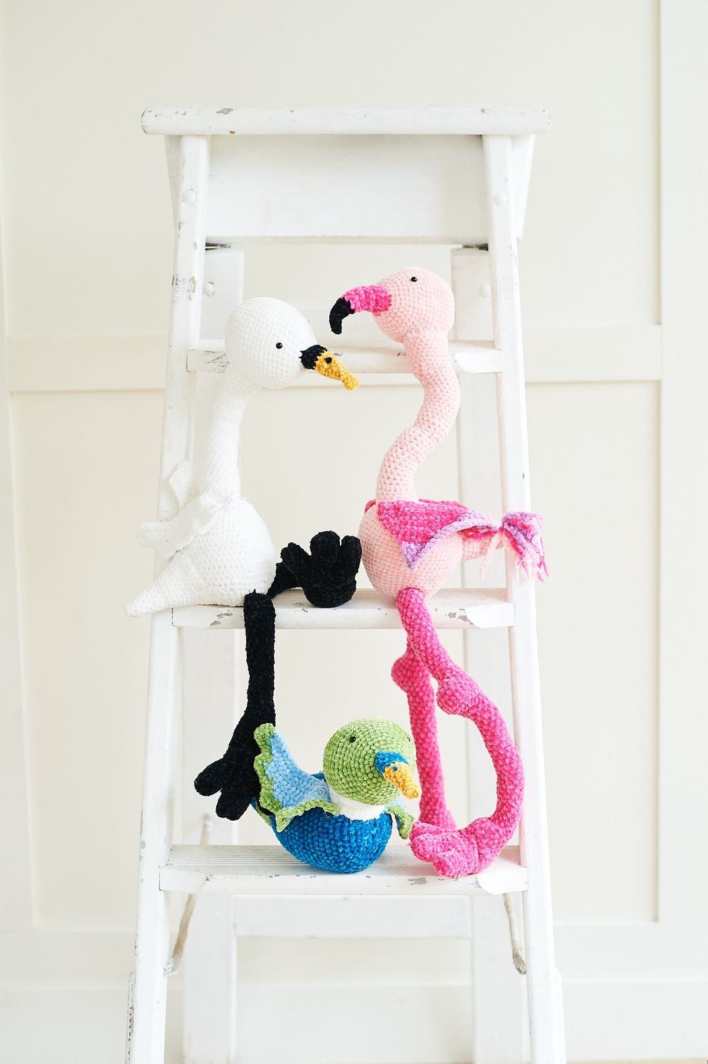 A pink crocheted flamingo, a white with black crocheted swan and a blue and green crocheted duck.