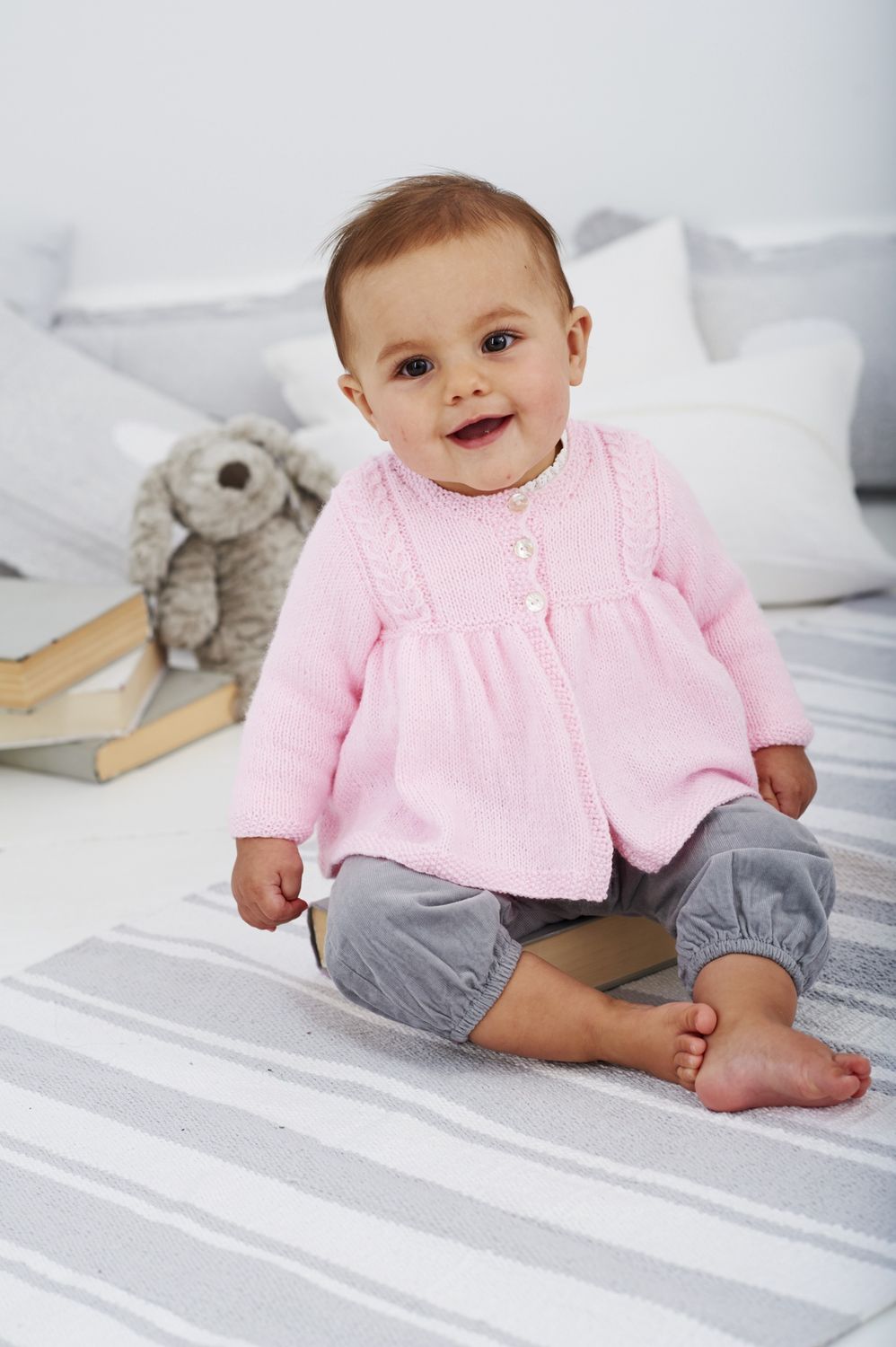 A baby is wearing a pink knitted coat.