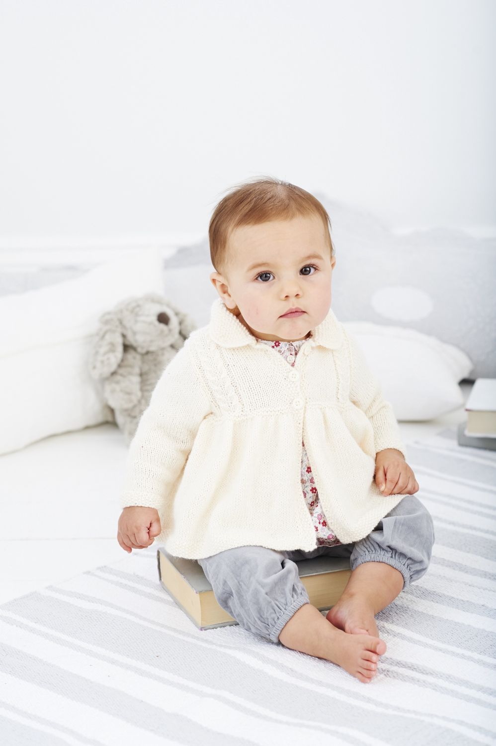 A baby is wearing a cream knitted coat.