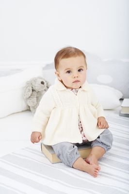 A baby is wearing a cream knitted coat.