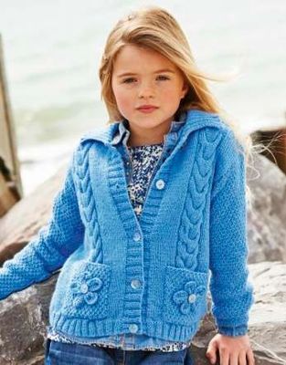 A girl is wearing a blue cable knit cardigan with flower motif pockets.