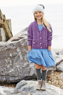 A girl is wearing a purple cable knit cardigan with flower motif pockets.
