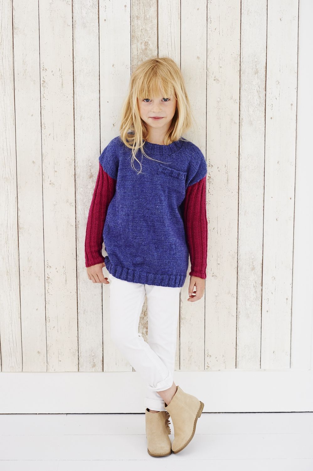 A girl is wearing a blue knitted sweater with dark pink sleeves.