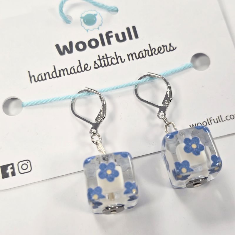 2 clear cube shaped stitch markers with blue flowers printed on.