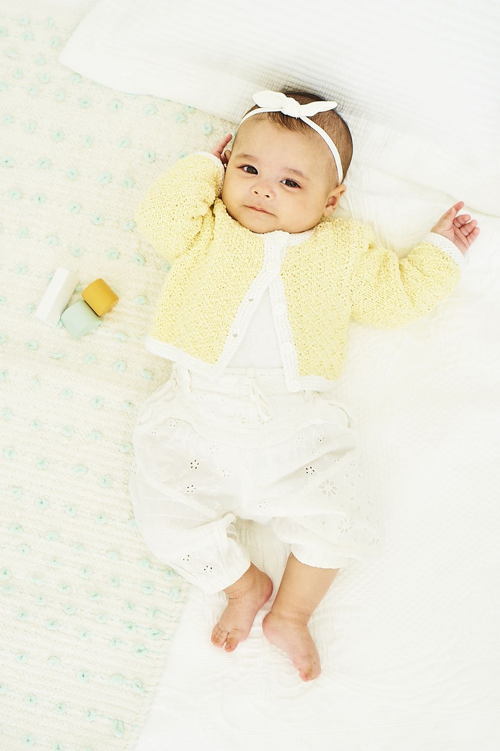 A baby is wearing a yellow knitted cardigan.