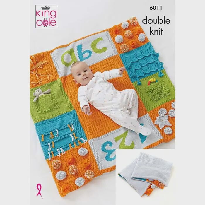A baby is laying on an orange, blue, grey and green knitted play mat.