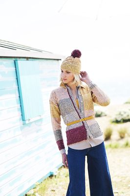 A woman is wearing a knitted cardigan in pink, red, yellow and grey stripes with a matching hat.