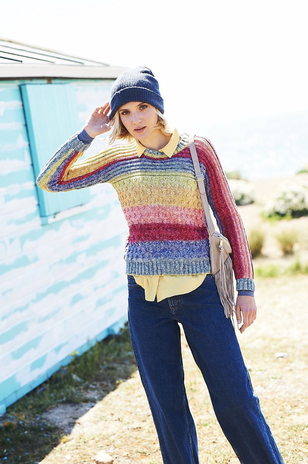 A woman is wearing a knitted sweater in red, coral, yellow, green and blue stripes.