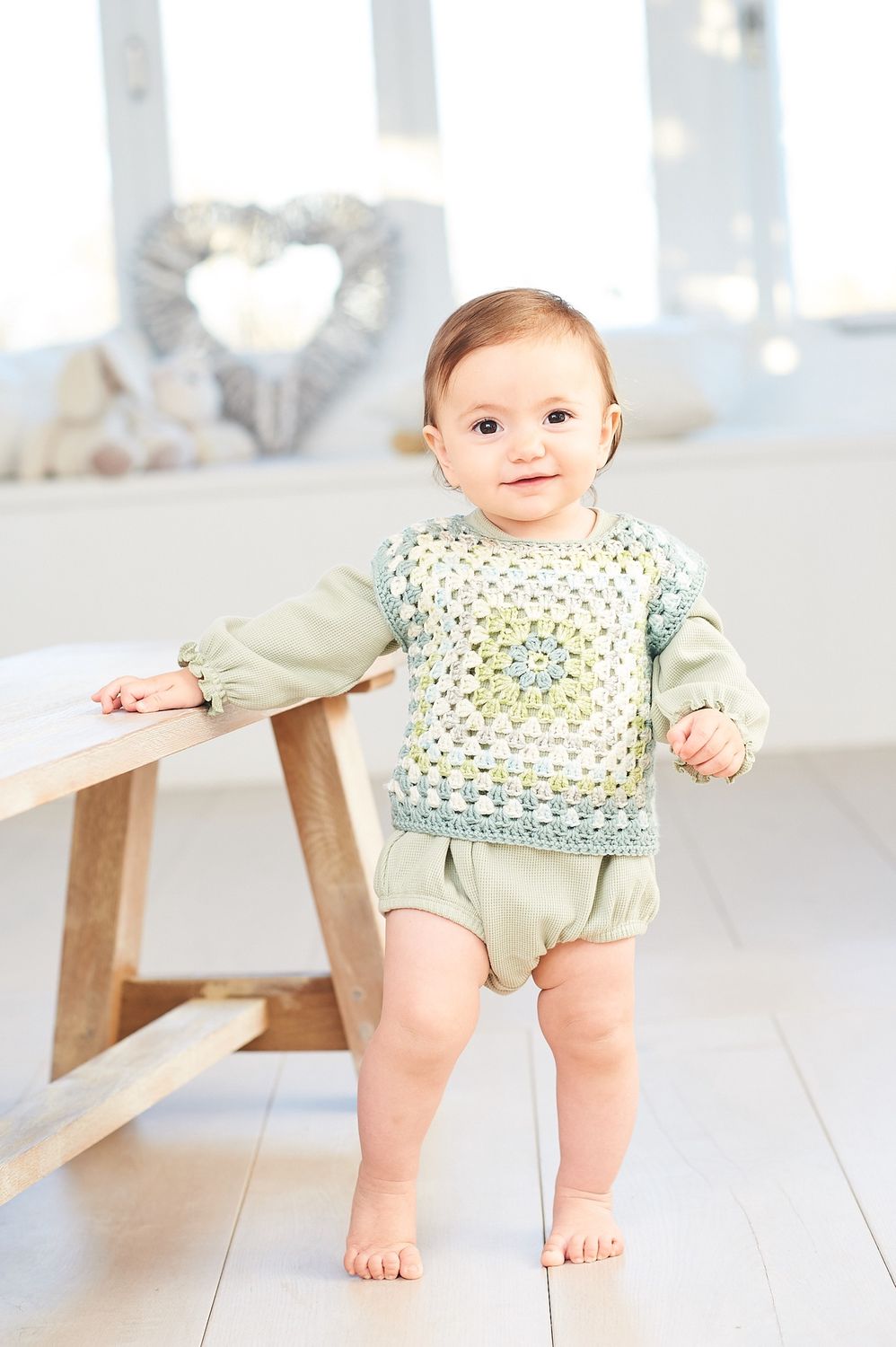 A baby is wearing a variegated green crocheted top.