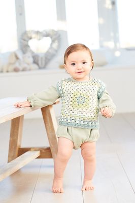 A baby is wearing a variegated green crocheted top.