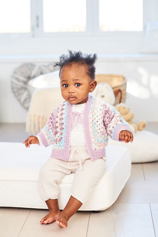 A baby is wearing a variegated pink crocheted cardigan.