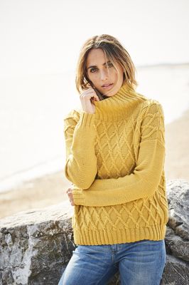 A woman is wearing a mustard yellow knitted sweater with diamond shaped cable detail.