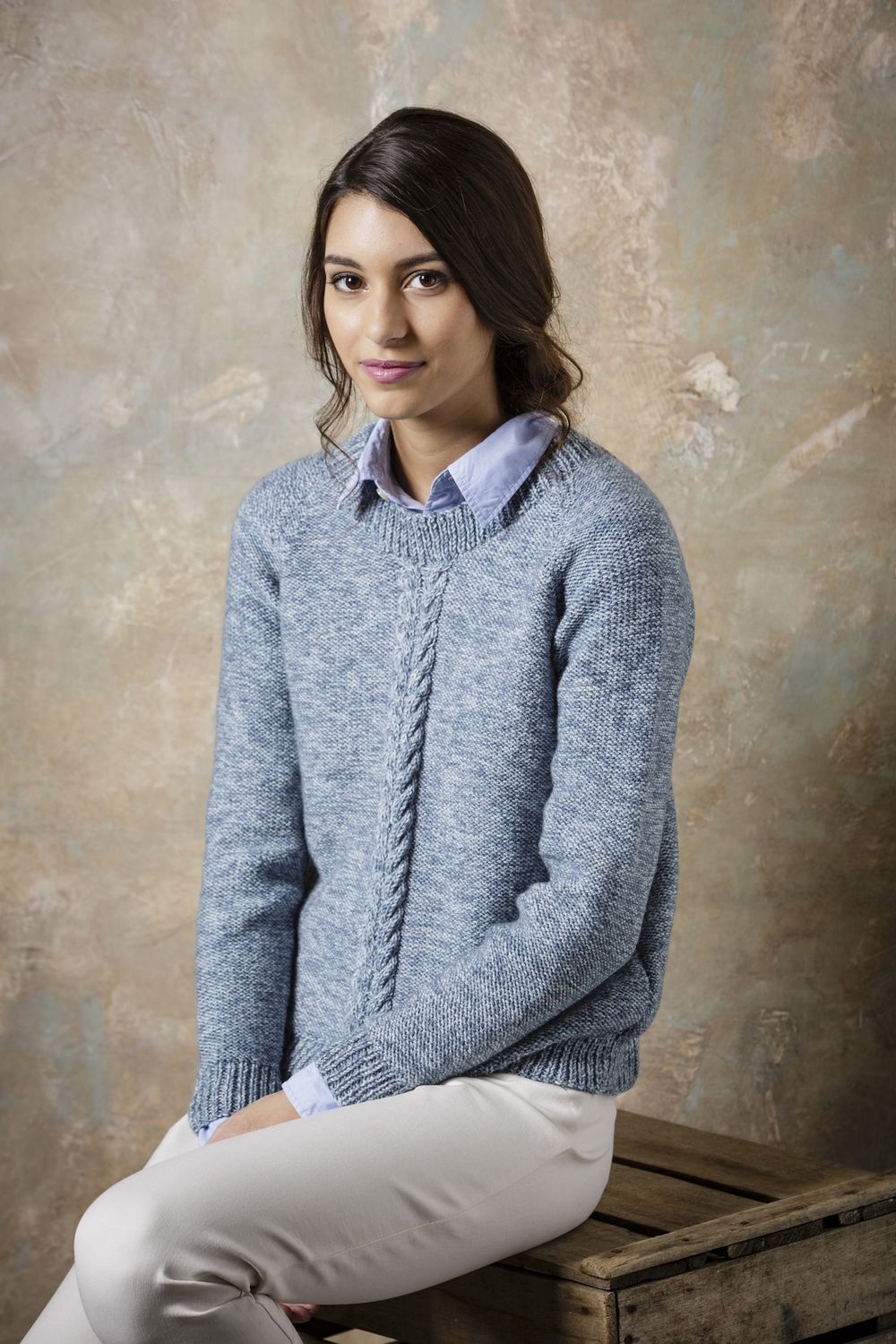 A woman is wearing a pale blue knitted sweater with cable detail down the front.
