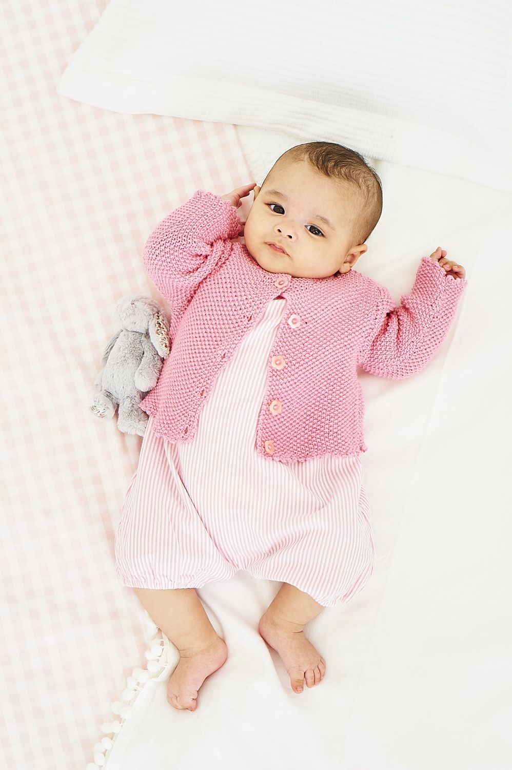 A baby is wearing a pink knitted cardigan.
